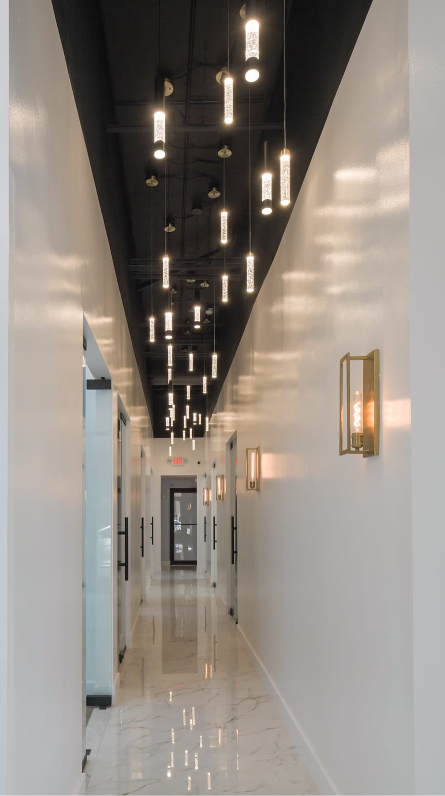 The suite corridor at the Bethesda building: a run of numbered doors under a line of pendant lights, reflected in a polished calacatta floor.