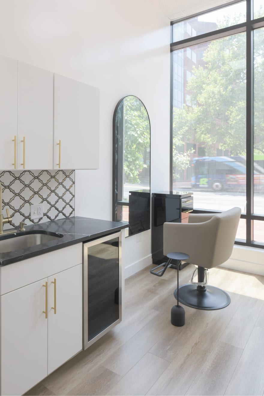A suite at the Bethesda building: a styling chair and mirror beside a full-height window, with a white counter and cabinetry along the wall.